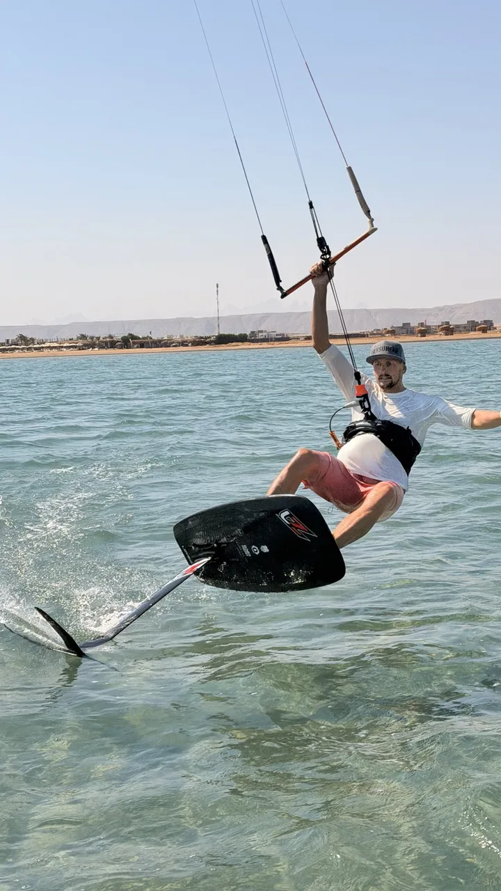 Kitefoiler vyskakuje z laguny s rovnou vodou v El Gouně na foilu Levitaz, v pozadí město a hory