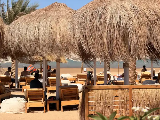 Lounge paluba se slaměnou střechou v SALT El Gouna — dřevěná lehátka a hosté s výhledem na kite lagunu