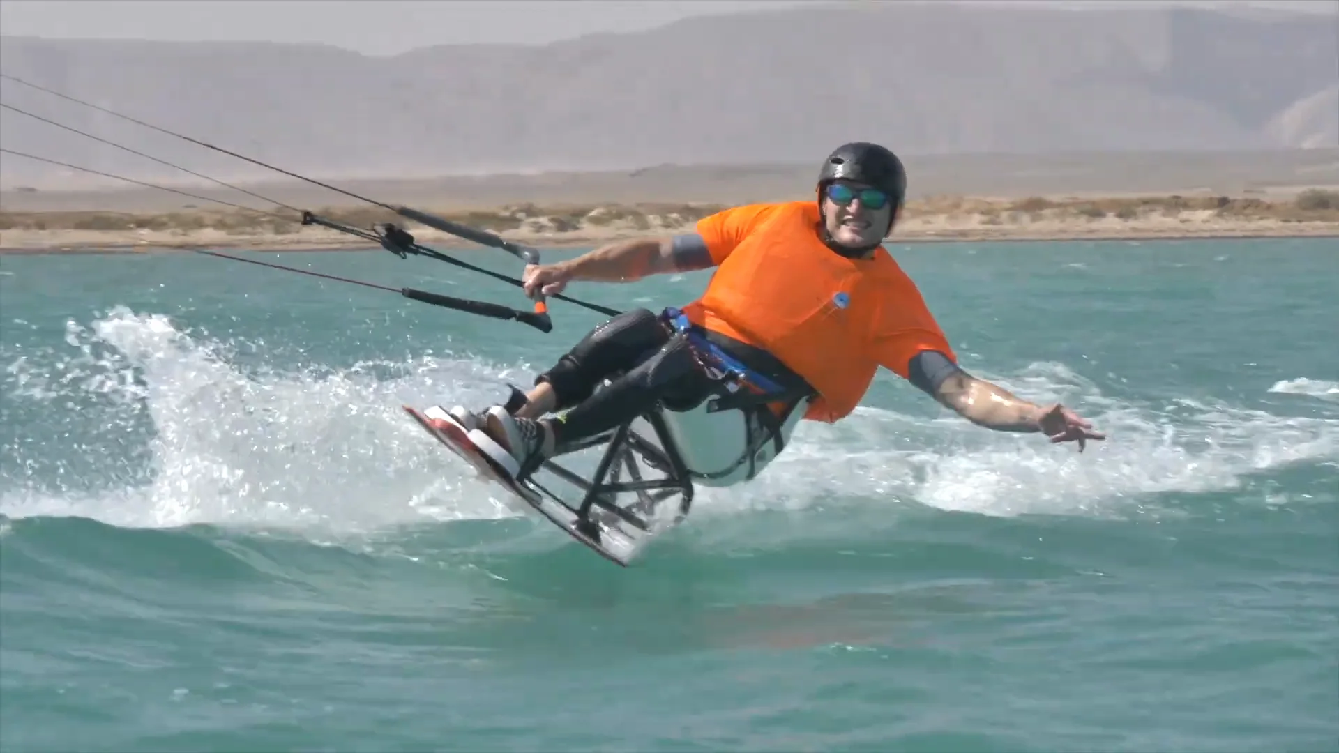 Sit-kitesurfer řeže vodu u El Gouny, jede vsedě v konstrukci a v jedné ruce drží bar kitu
