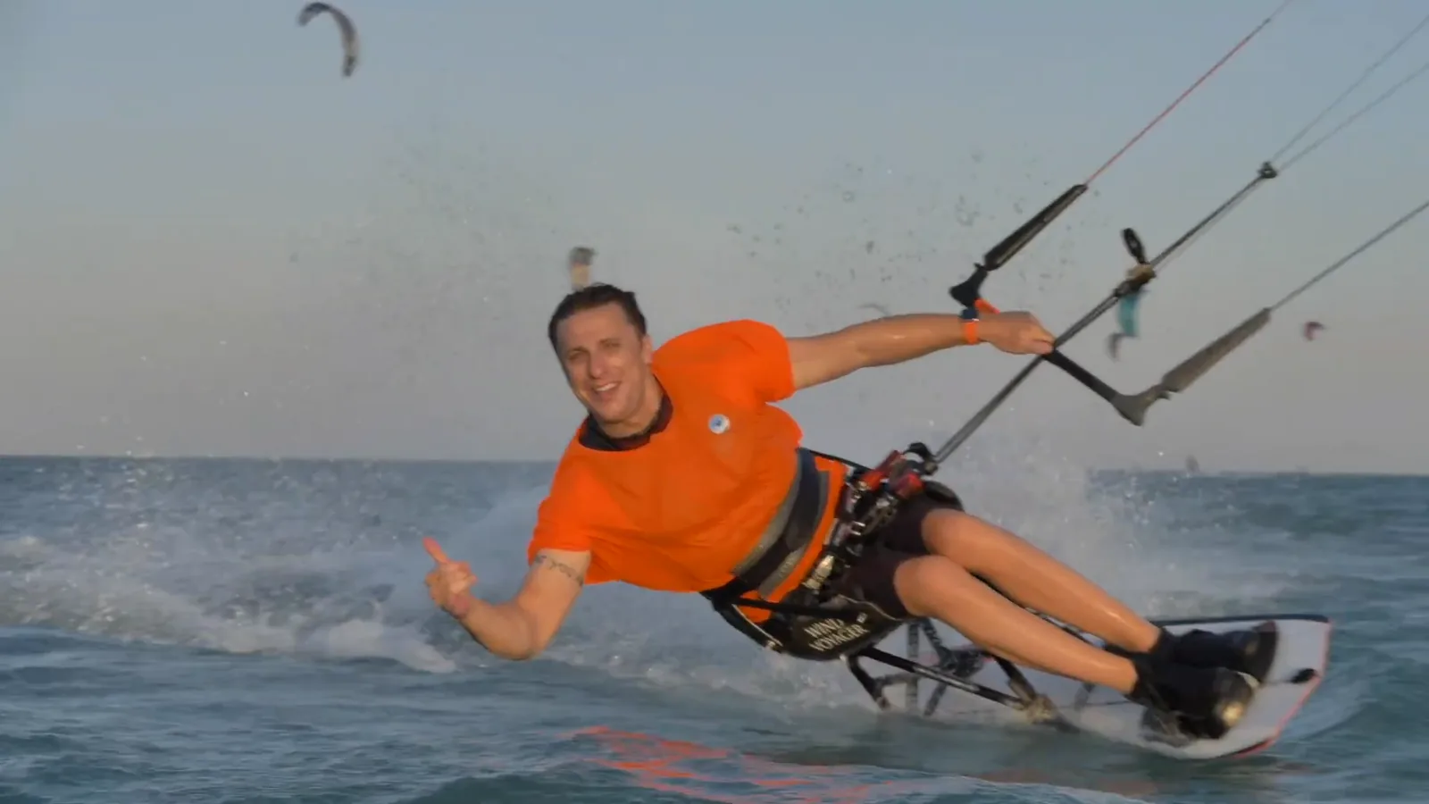 Sit-kitesurfer jede směrem ke kameře, palec nahoru a široký úsměv